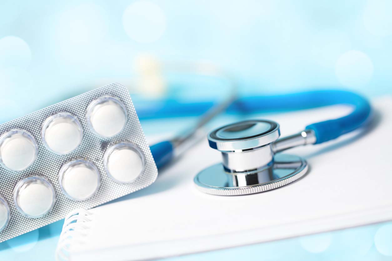 Medical concept - stethoscope with some pills on a spiral notebook